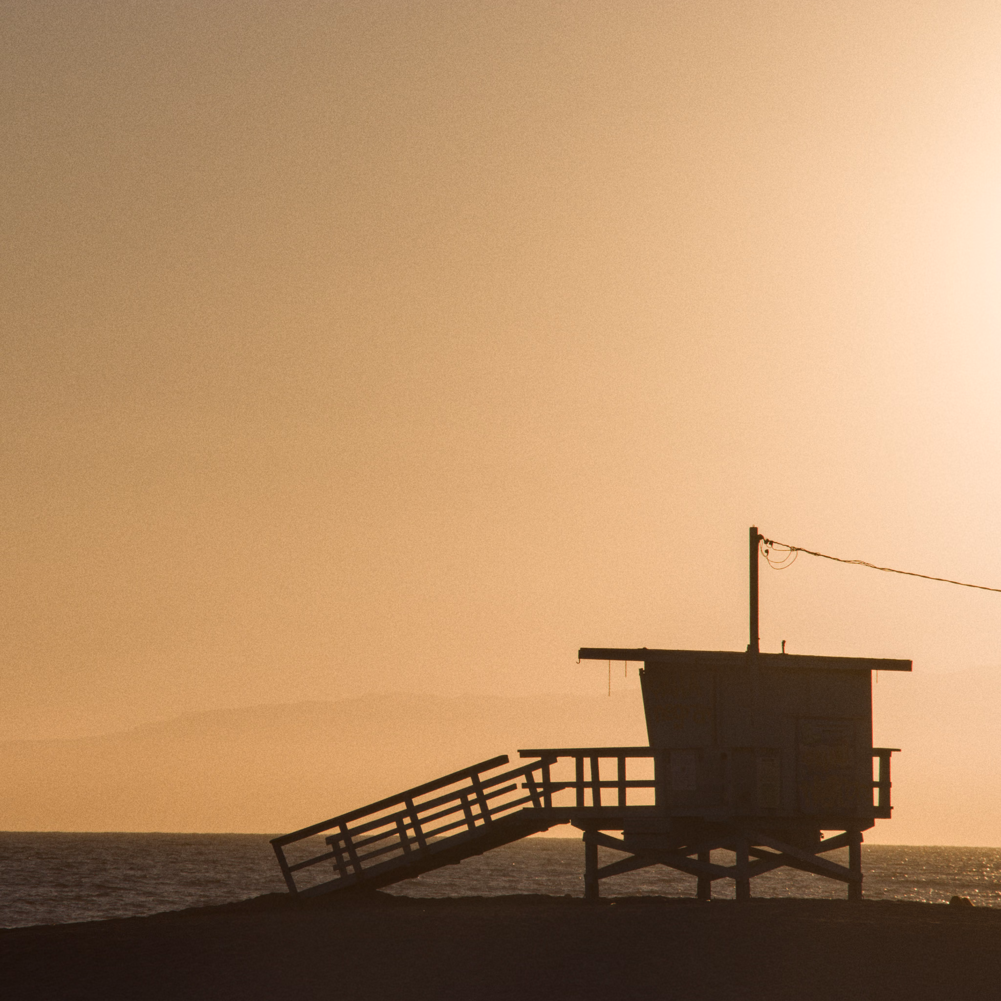 A lifeguard tower in silhouette against a hazy sunset over the sea